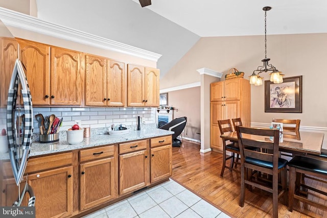 kitchen featuring lofted ceiling, stainless steel refrigerator, hanging light fixtures, tasteful backsplash, and light stone countertops