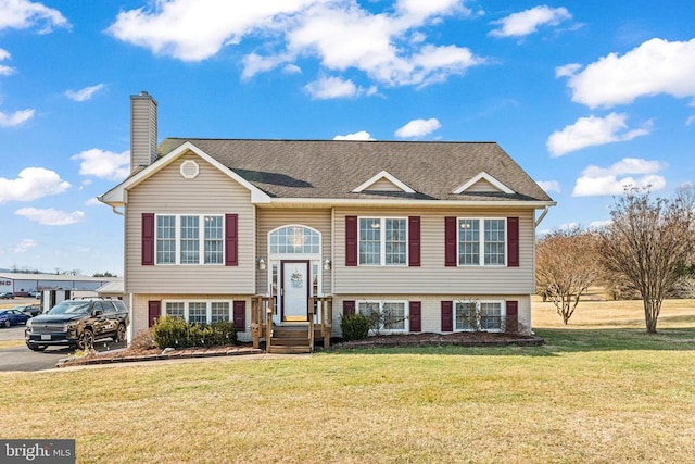 bi-level home featuring a front lawn, a chimney, a shingled roof, and brick siding