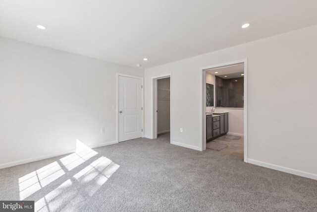 unfurnished bedroom featuring light carpet, ensuite bath, a walk in closet, and a closet