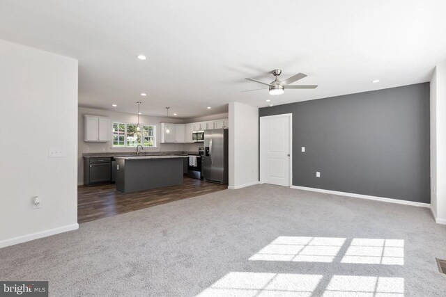 unfurnished living room featuring sink, dark carpet, and ceiling fan