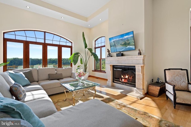 living room with a high end fireplace, a high ceiling, and light wood-type flooring