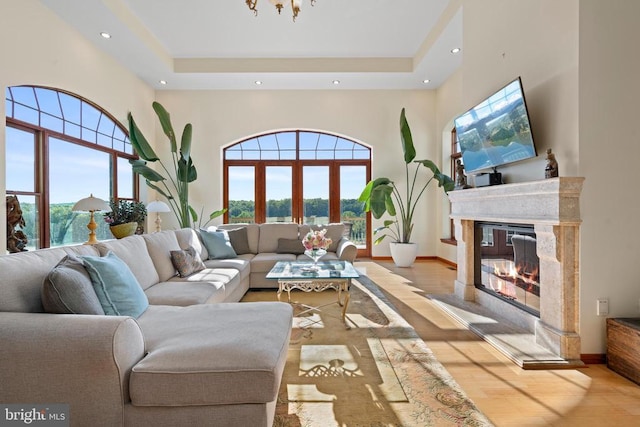 living room with a tray ceiling, a fireplace, a high ceiling, and light wood-type flooring