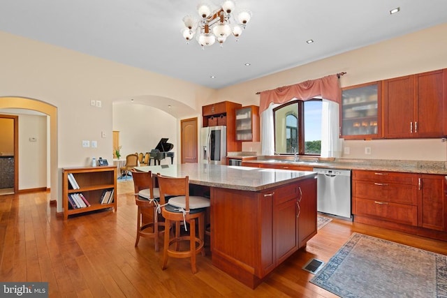 kitchen with a kitchen island, appliances with stainless steel finishes, a chandelier, light hardwood / wood-style floors, and light stone countertops