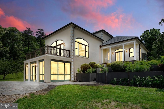 back house at dusk with a balcony and a lawn