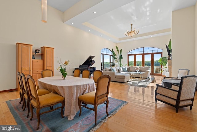 dining space with a raised ceiling, a high ceiling, a chandelier, and light wood-type flooring