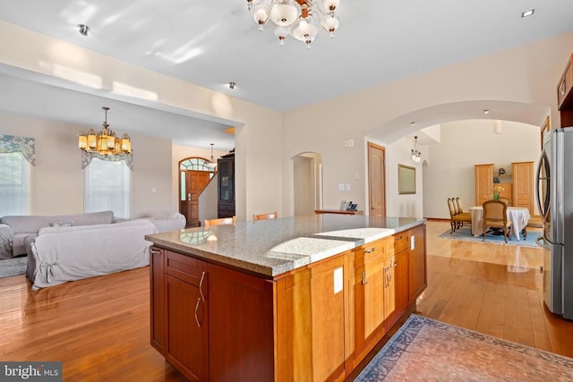 kitchen with light stone counters, a notable chandelier, stainless steel refrigerator, and light wood-type flooring