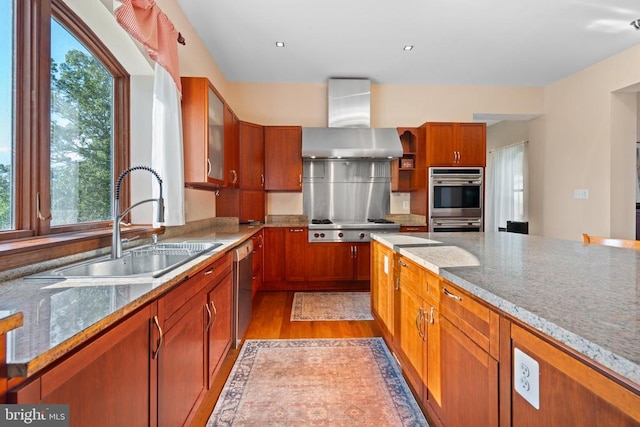 kitchen with wall chimney exhaust hood, sink, light stone counters, light wood-type flooring, and appliances with stainless steel finishes