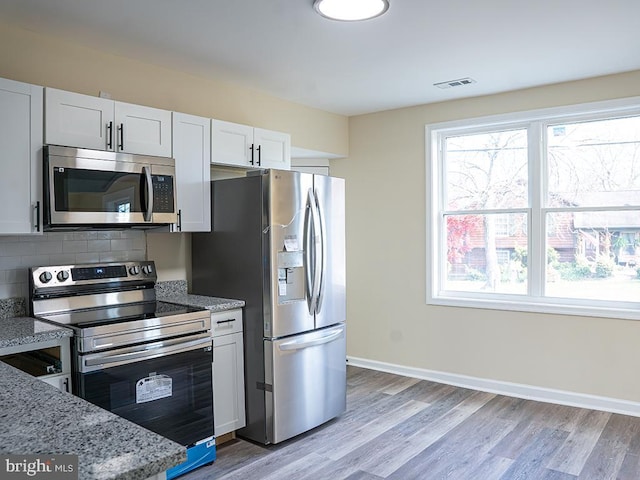 kitchen with stainless steel appliances, a wealth of natural light, light stone countertops, and white cabinets