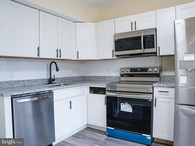 kitchen featuring sink, white cabinets, decorative backsplash, stainless steel appliances, and light stone countertops