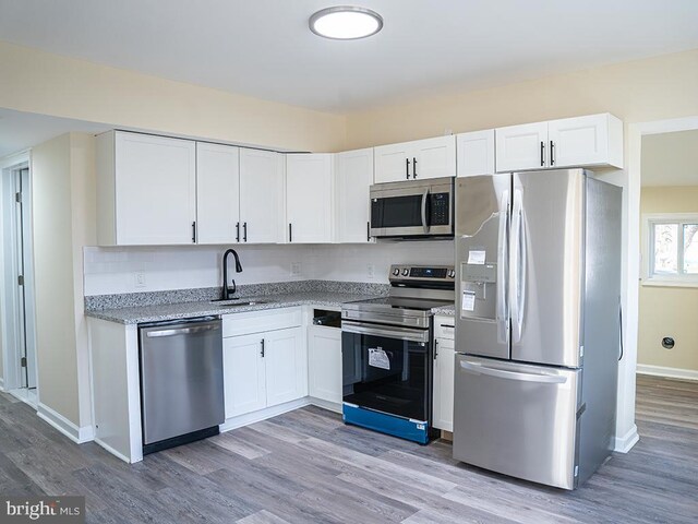 kitchen with stainless steel appliances, white cabinetry, sink, and light hardwood / wood-style flooring