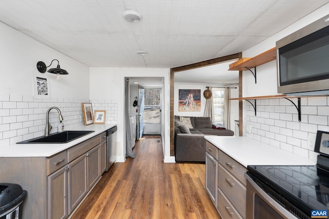 kitchen with open shelves, stainless steel appliances, light countertops, a sink, and wood finished floors