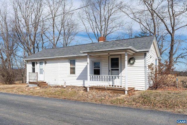 single story home featuring covered porch, roof with shingles, and a chimney