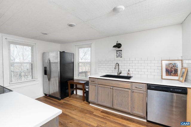 kitchen featuring decorative backsplash, wood finished floors, light countertops, stainless steel appliances, and a sink