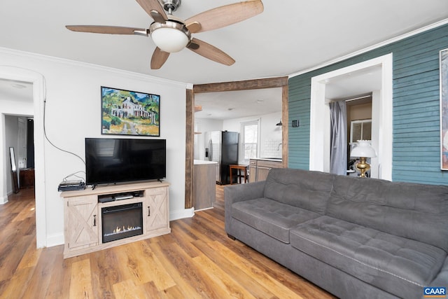 living area with baseboards, ornamental molding, and light wood-style floors