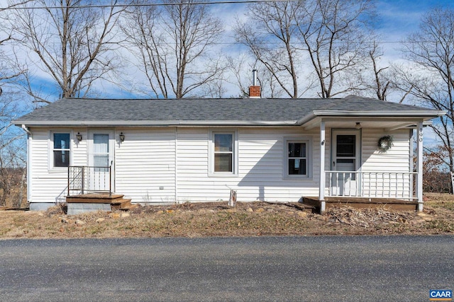 ranch-style house with a chimney, a porch, and roof with shingles