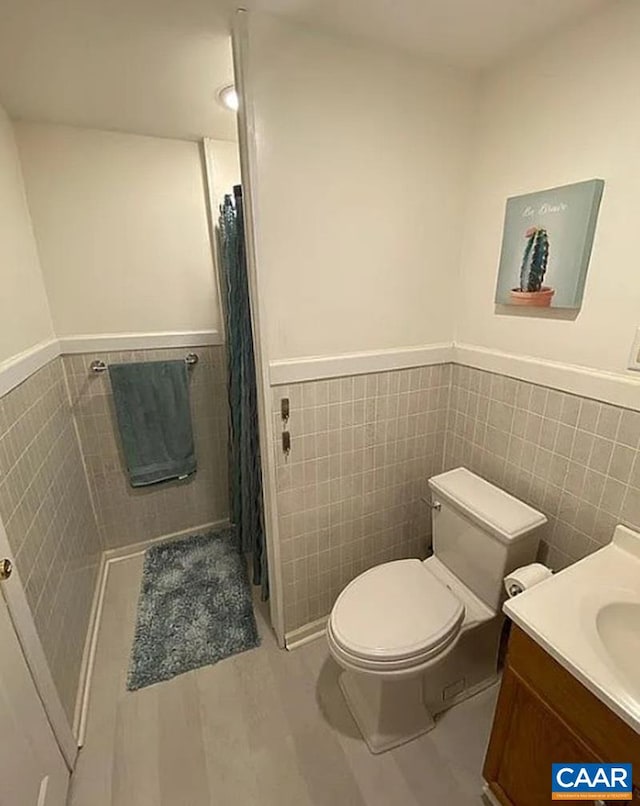 bathroom featuring a wainscoted wall, vanity, toilet, and tile walls