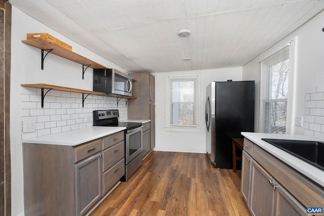 kitchen featuring tasteful backsplash, dark wood finished floors, appliances with stainless steel finishes, light countertops, and open shelves