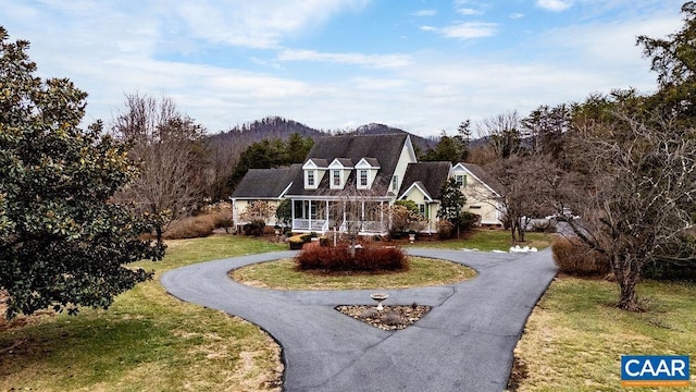 cape cod home featuring covered porch, driveway, and a front lawn