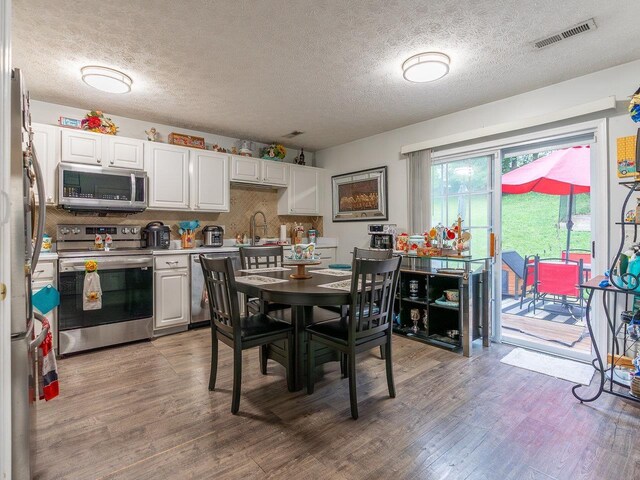 kitchen featuring appliances with stainless steel finishes, sink, backsplash, white cabinets, and light wood-type flooring