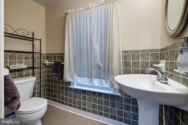 half bath with tile walls, toilet, a wainscoted wall, and tile patterned floors