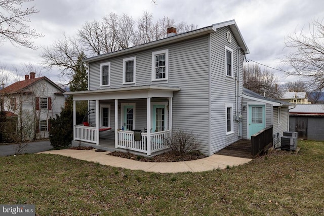 traditional home with central air condition unit, a porch, a chimney, and a front lawn