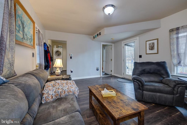 living area featuring stacked washer / drying machine, baseboards, and dark wood-style flooring