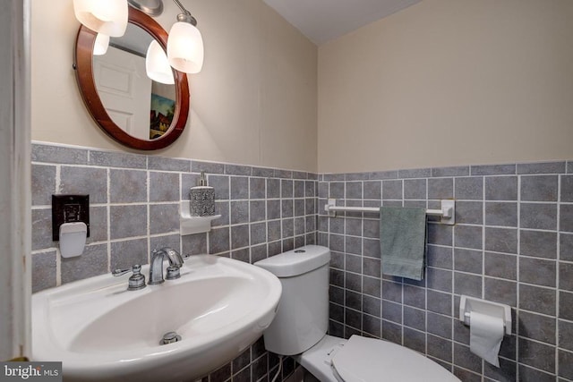 bathroom featuring a wainscoted wall, toilet, tile walls, and a sink