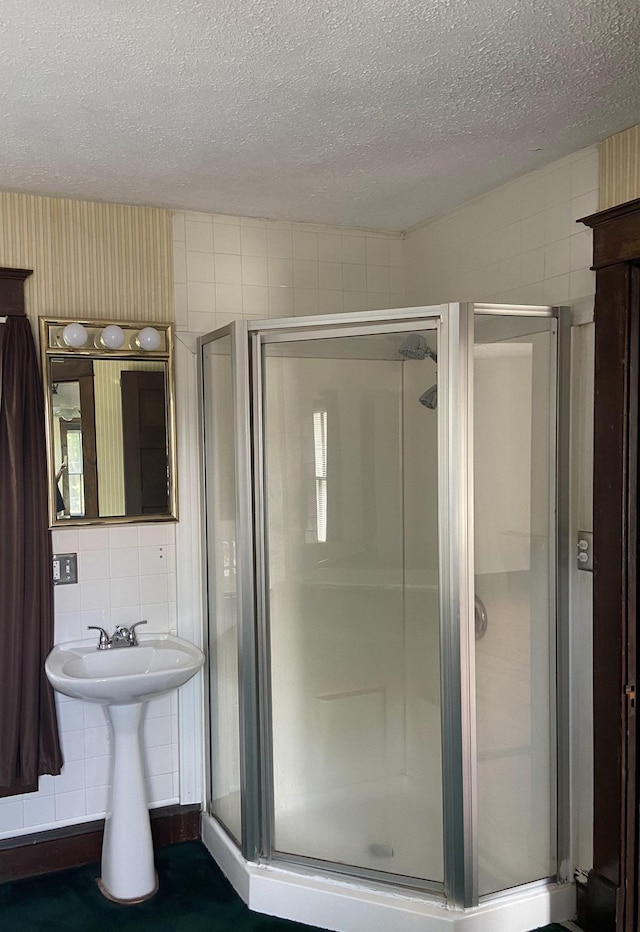 bathroom with walk in shower, sink, tile walls, and a textured ceiling