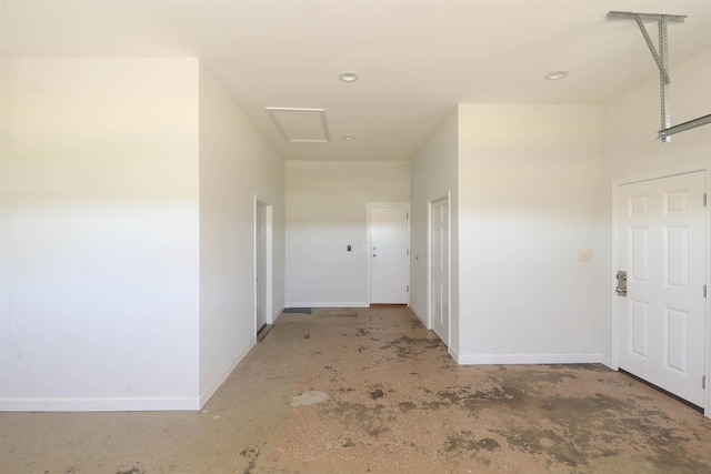 hallway with attic access, unfinished concrete floors, and baseboards