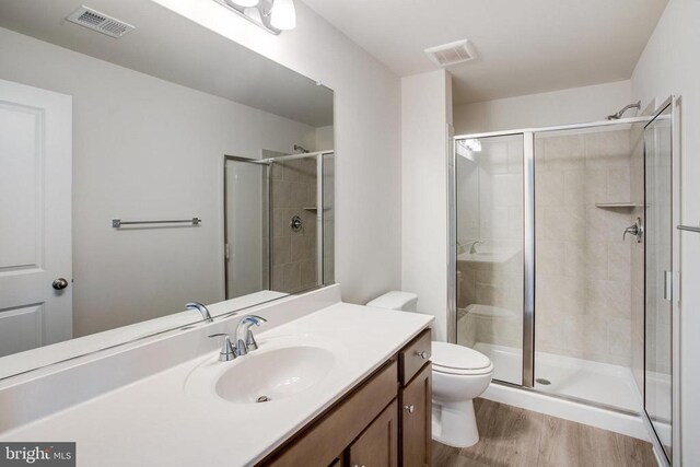 bathroom featuring vanity, hardwood / wood-style flooring, a shower with door, and toilet