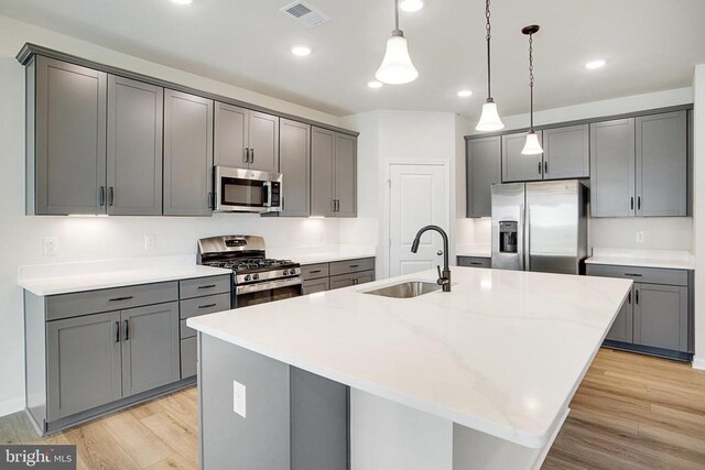 kitchen featuring stainless steel appliances, an island with sink, and gray cabinetry