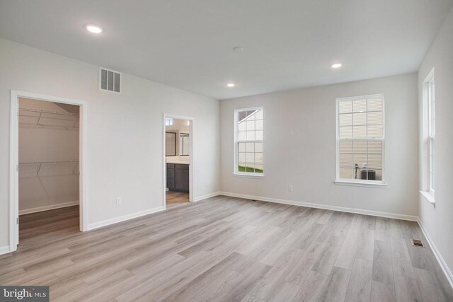 unfurnished bedroom featuring a closet, ensuite bathroom, a spacious closet, and light hardwood / wood-style flooring