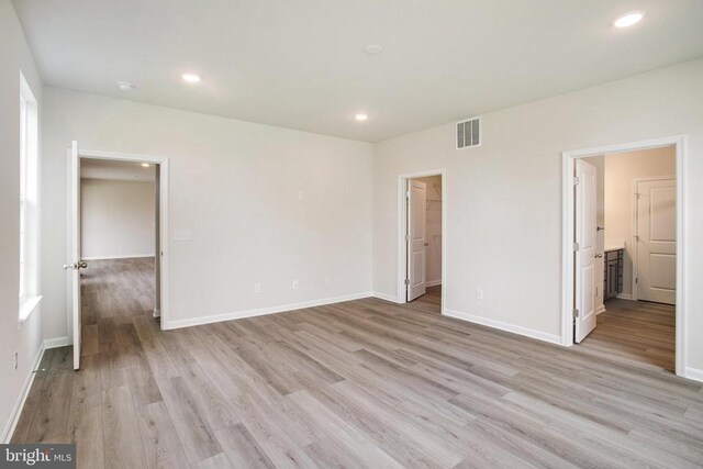 unfurnished bedroom featuring ensuite bathroom, a spacious closet, and light hardwood / wood-style flooring