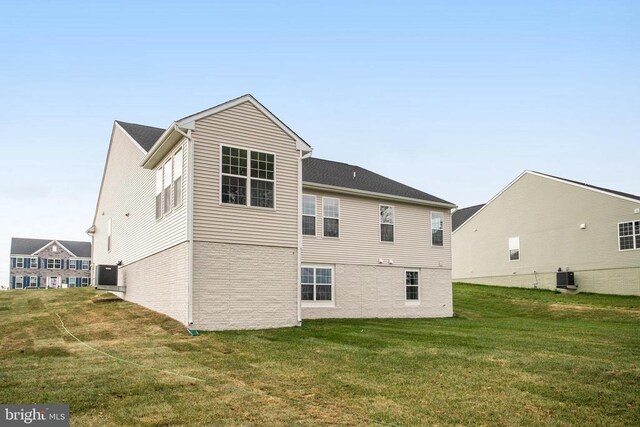 rear view of house with central AC unit and a lawn