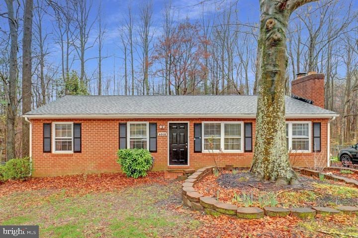 ranch-style home with brick siding, a chimney, and a shingled roof