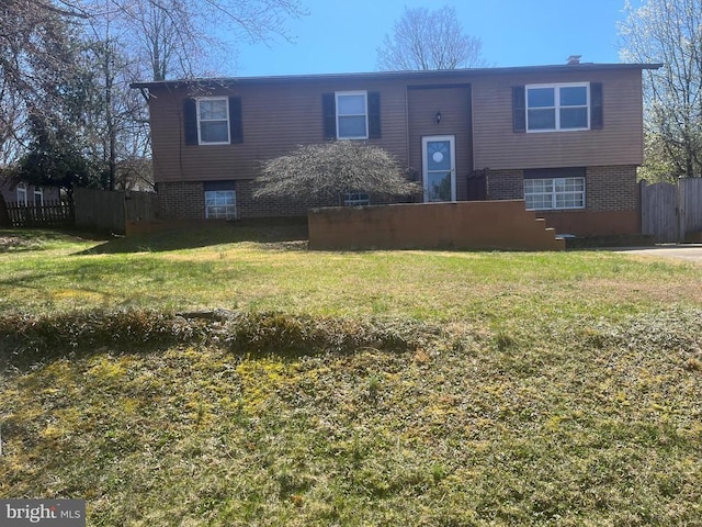 split foyer home featuring brick siding, a front lawn, and fence