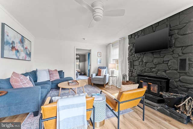 living room with ornamental molding, ceiling fan, a stone fireplace, and wood finished floors