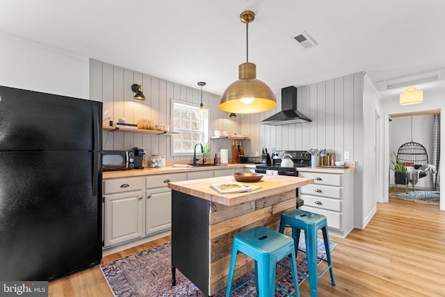 kitchen with butcher block countertops, a sink, electric stove, wall chimney range hood, and freestanding refrigerator