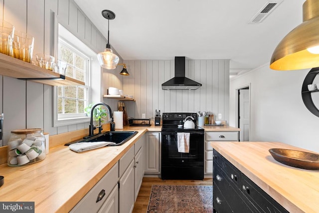 kitchen featuring black electric range, visible vents, a sink, wood counters, and wall chimney range hood