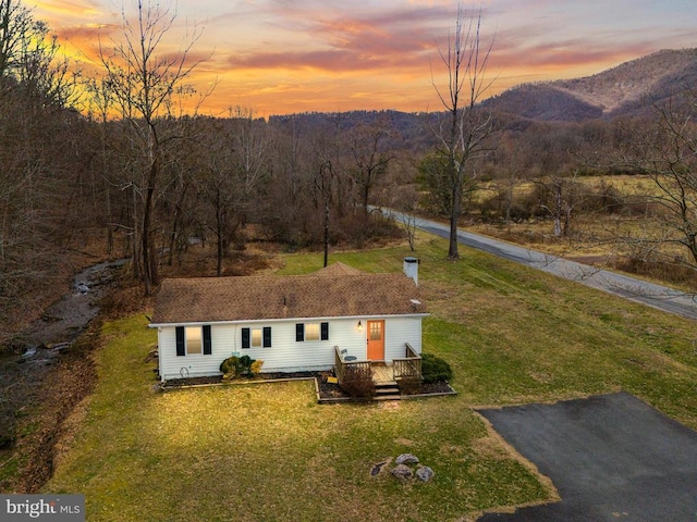 view of front of house featuring a yard, a deck with mountain view, and a wooded view