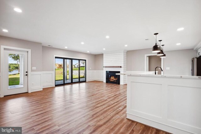 kitchen with a fireplace, stainless steel fridge, hanging light fixtures, and light wood-type flooring