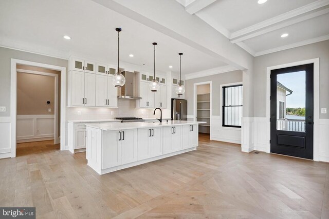 kitchen with white cabinetry, hanging light fixtures, stainless steel fridge with ice dispenser, a center island with sink, and wall chimney range hood