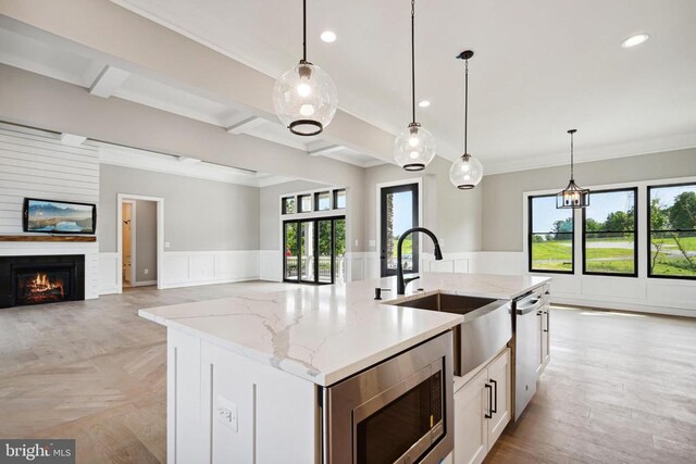 kitchen featuring pendant lighting, appliances with stainless steel finishes, light stone countertops, and a center island with sink