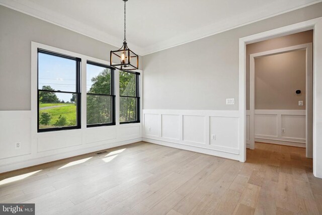 unfurnished dining area with an inviting chandelier, crown molding, and light wood-type flooring