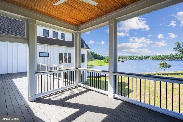 wooden deck with a water view, ceiling fan, and a yard