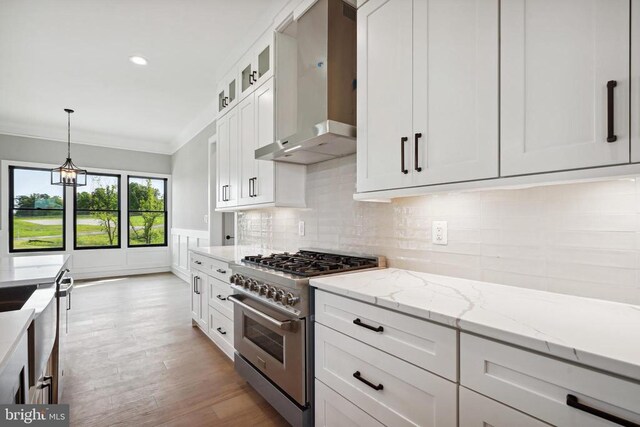 kitchen featuring pendant lighting, white cabinets, high end stainless steel range oven, crown molding, and wall chimney exhaust hood