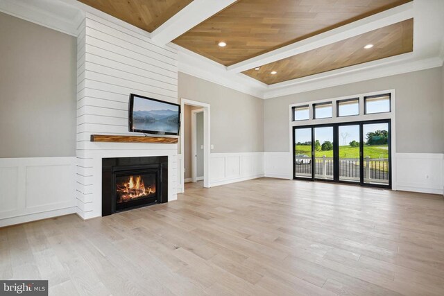 unfurnished living room featuring a large fireplace, light wood-type flooring, ornamental molding, wooden ceiling, and beam ceiling