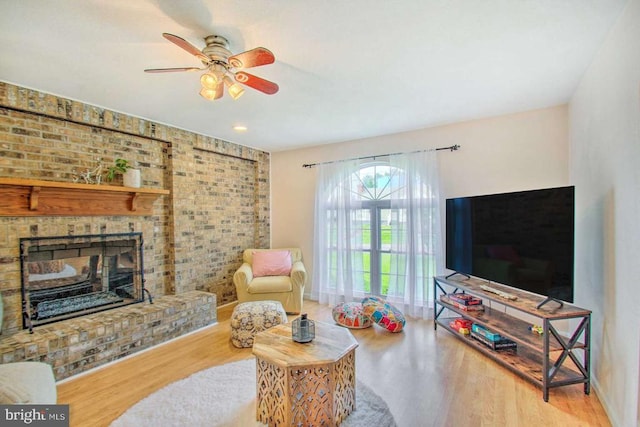 living area featuring a brick fireplace, brick wall, a ceiling fan, and wood finished floors