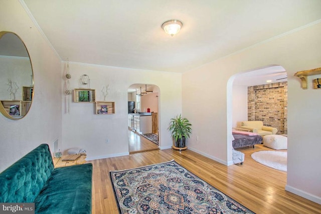 living area with crown molding, wood finished floors, arched walkways, and baseboards