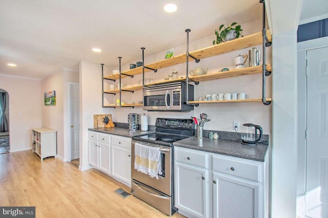 kitchen featuring dark countertops, light wood-type flooring, appliances with stainless steel finishes, white cabinetry, and open shelves